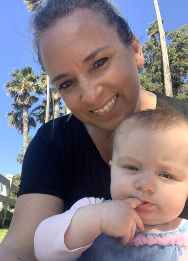 smiling woman with infant girl, outside with palm trees in the background